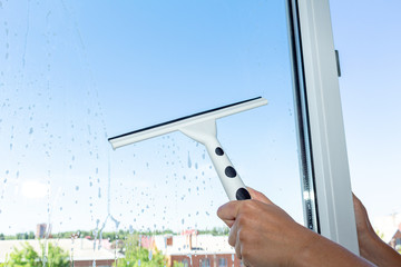 Washing cleaning windows by cleaning service hand with a special brush squeegee window cleaner on a blue sky background