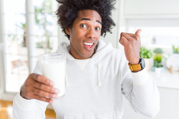 African American man holding and drinking glass of milk pointing and showing with thumb up to the side with happy face smiling