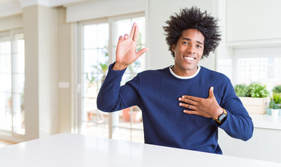 Young african american man wearing casual sweater sitting at home smiling swearing with hand on...