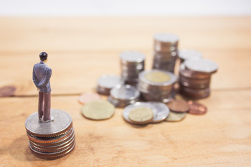 Miniature businessman stand on coins on wooden table. business planning concept.