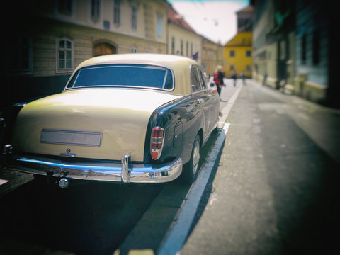 A parked old car from the sixties in the city street, blurred image.