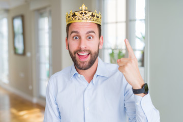 Handsome business man wearing golden crown as a king or prince pointing finger up with successful...