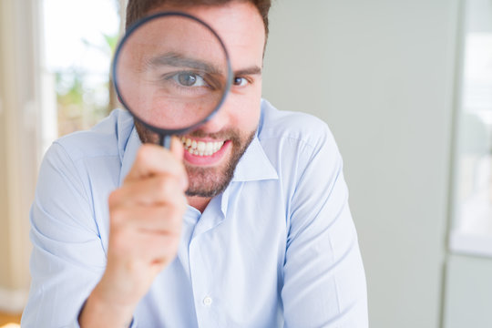 Handsome business man holding magnifying glass close to face, big eyes and funny expression