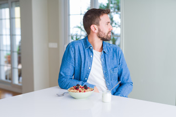 Handsome man eating cereals for breakfast at home looking to side, relax profile pose with natural face with confident smile.