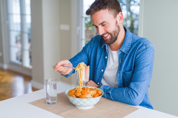 Handsome man eating pasta with meatballs and tomato sauce at home while smiling at the camera