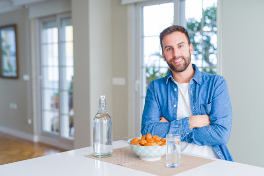 Handsome man eating pasta with meatballs and tomato sauce at home happy face smiling with crossed arms looking at the camera. Positive person.