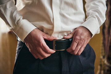 Businessman putting on a belt, fashion and clothing concept,groom getting ready in the morning...