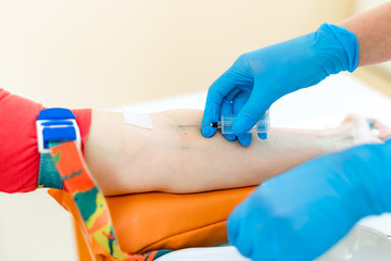 Nurse is pricking needle for the syringe into the patient's arm to take blood sample in a lab....