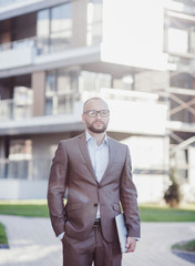 Confident young man in full suit looking at camera standing outdoors with cityscape