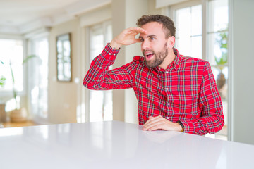 Handsome man wearing colorful shirt very happy and smiling looking far away with hand over head. Searching concept.