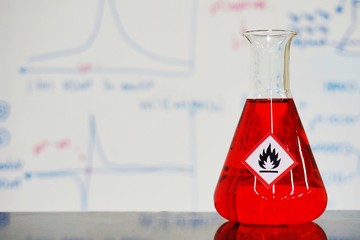 Erlenmeyer flask with Red liquid and chemical hazard warning symbols labels (flammable sign) on...