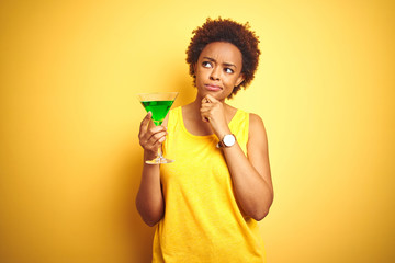 Young african american woman with afro hair drinking a cocktail over yellow isolated background serious face thinking about question, very confused idea