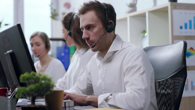 Close up view of angry and nervous call center operator with headset talking with the hotline customer, being irritated, uses bubble wrap to calm down and continues conversation. Stressful situation
