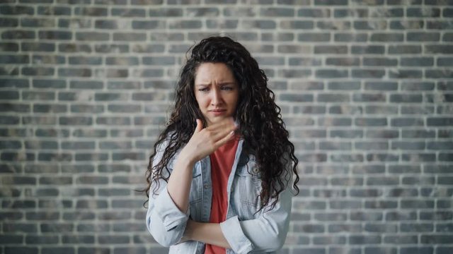 Pretty young woman with long curly hair is holding nose because of disgusting smell and frowning suffering from stench. People and negative reaction concept.
