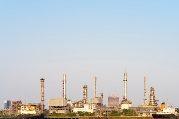 Crude oil refinery plant and many chimney with petrochemical tanker or cargo ship at coast of river on sky afternoon  bright day at thailand with copy space