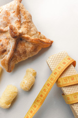 yellow plastic measuring tape on the background of white waffles and other bakery products, vertical image. fighting overweight, overeating and obesity during the diet
