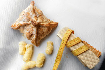 A yellow measuring tape wrapping waffles, baked apple pie and sweet corn sticks on the gray background. healthy life style, weight loss concept image.