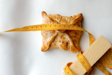 Yellow Plastic tape measure on the white waffles and baked apple pie. fitness, nutritionist, dietitian, fighting diabetes, obesity and cholesterol.