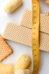 yellow plastic measuring tape on the background of white waffles and other bakery products, vertical image. measuring tape in diet concept. dietary for slim shape concept.