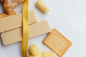 blank yellow plastic tape measure on the background of white waffles, cookies, sweet corn sticks and other confectionery. Sweet, dessert, diet concept.