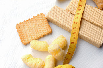 counting calories during a diet: yellow plastic measuring tape on the background of white waffles, cookies, sweet corn sticks. addiction to sweets and pastries. .