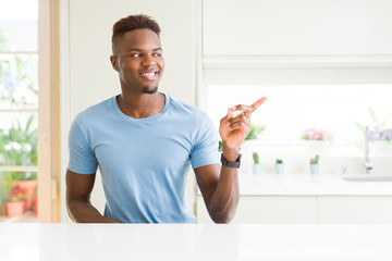 Handsome african american man wearing casual t-shirt at home with a big smile on face, pointing with hand and finger to the side looking at the camera.