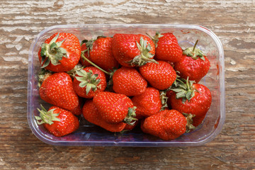 flat lay of fresh and ripe strawberries in plastic transparent container box, which lies on a wooden background. time to harvest strawberries in the garden