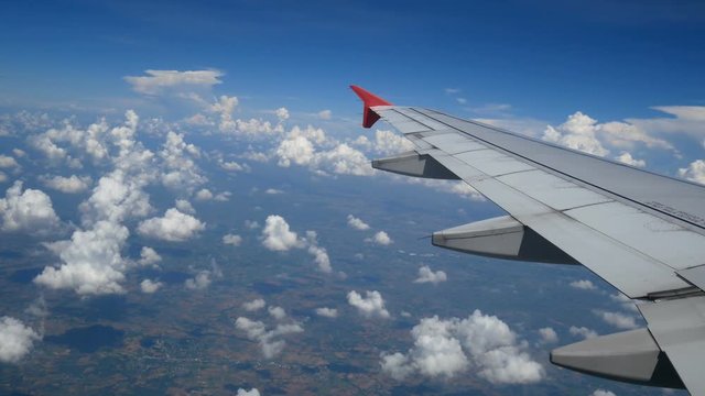 4K footage. traveling by air. aerial view through an airplane window. wing airplane and beautiful white clouds in blue sky for travel background