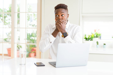 African american business man working using laptop shocked covering mouth with hands for mistake. Secret concept.