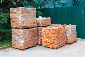 packs of orange bricks in the plastic protective film are near the construction site. construction...