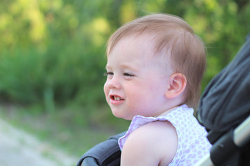little, beautiful, smiling, cute redhead baby in a pram out-of-doors in a sleeveless shirt