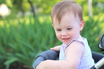 little, beautiful, smiling, cute redhead baby in a pram out-of-doors in a sleeveless shirt looking down