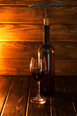 Bottle of red wine with a glass and corkscrew on an old wooden table.Candle light.