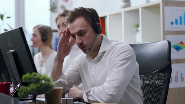Close up view of angry and nervous call center operator with headset talking with the hotline customer, being irritated, uses bubble wrap to calm down and continues conversation. Stressful situation