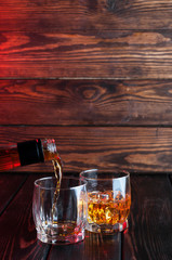Pouring whiskey in the two glasses with ice cubes on wood table.Studio photography.