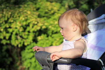 little, beautiful, smiling, cute redhead baby in a pram out-of-doors in a sleeveless shirt looking ahead