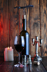 Bottle of red wine with a glass and corkscrew on an old wooden table.Candle light.