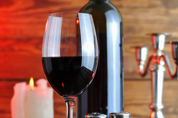 A glass of red wine with a bottle and a  candle on a wooden background.Candle light.