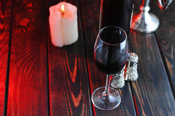 A glass of red wine with a bottle and a  candle on a wooden background.Candle light.