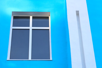 abstract photo of a darkened window with a partition cross on a blue wall and a white rectangular column
