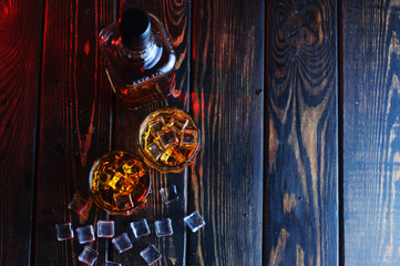 Two glasses of whiskey with ice cubes served on wooden planks.