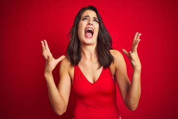 Beautiful woman wearing bikini swimwear over red isolated background crazy and mad shouting and yelling with aggressive expression and arms raised. Frustration concept.