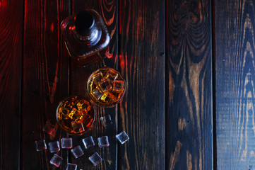 Two glasses of whiskey with ice cubes served on wooden planks.