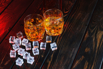 Two glasses of whiskey with ice cubes served on wooden planks.