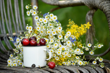 Summer simple still life. Sweet cherry in an iron mug and a simple bouquet of summer field flowers. Vintage style. summer on the farm.