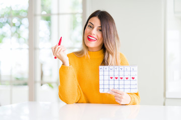 Young beautiful woman holding menstruation calendar at home with a happy face standing and smiling with a confident smile showing teeth