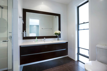 Big mirror with white and luxurious interior of the bathroom. Vase of flowers above the sink