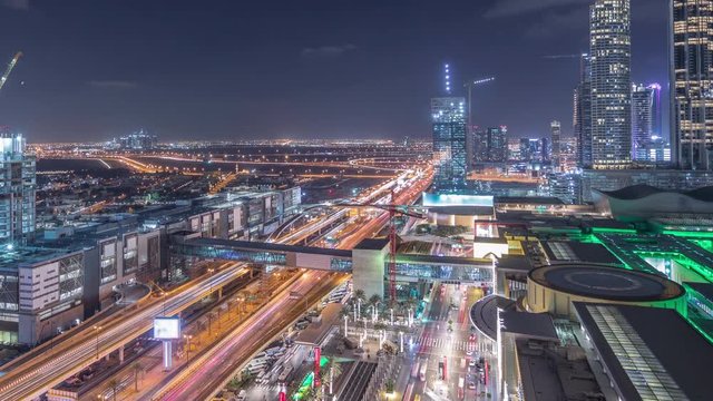 Aerial view of Financial center road night timelapse with shopping mall and under construction building with cranes from downtown, Dubai Creek harbor on background