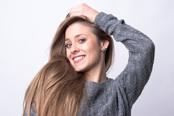 Beauty portrait of young cute woman with long healthy hair posing and smiling on light gray background. 