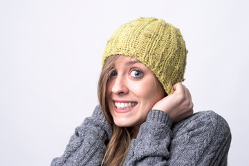 Portrait of freezing young woman with yellow beanie covering head on cold winter weather on light gray background. 